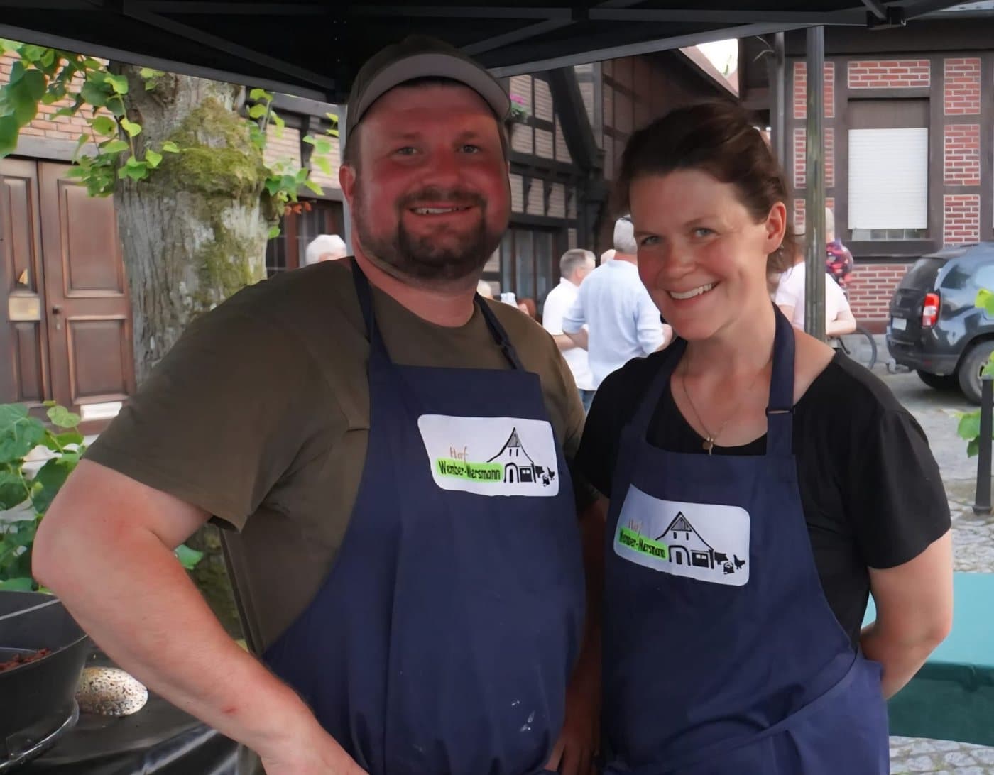 Anne Wember-Mersmann und ihr Mann in Schürzen mit dem Hoflogo an ihrem Stand